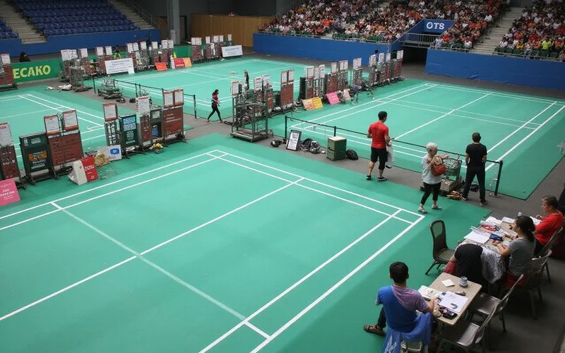 Multiple badminton courts set up for a tournament with scoreboards and seating arranged along the sidelines